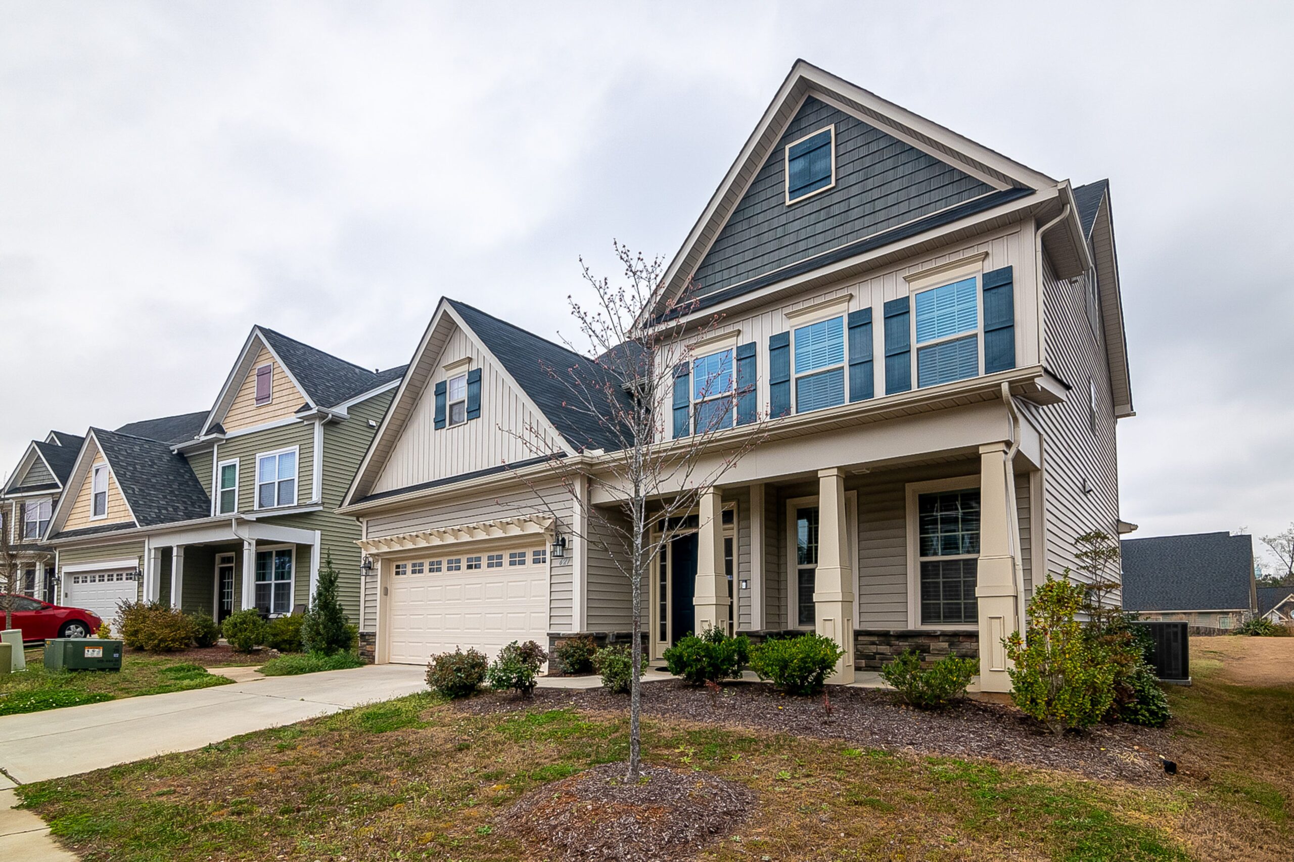 A row of modern suburban homes with garages, driveways, and landscaped lawns in daylight.